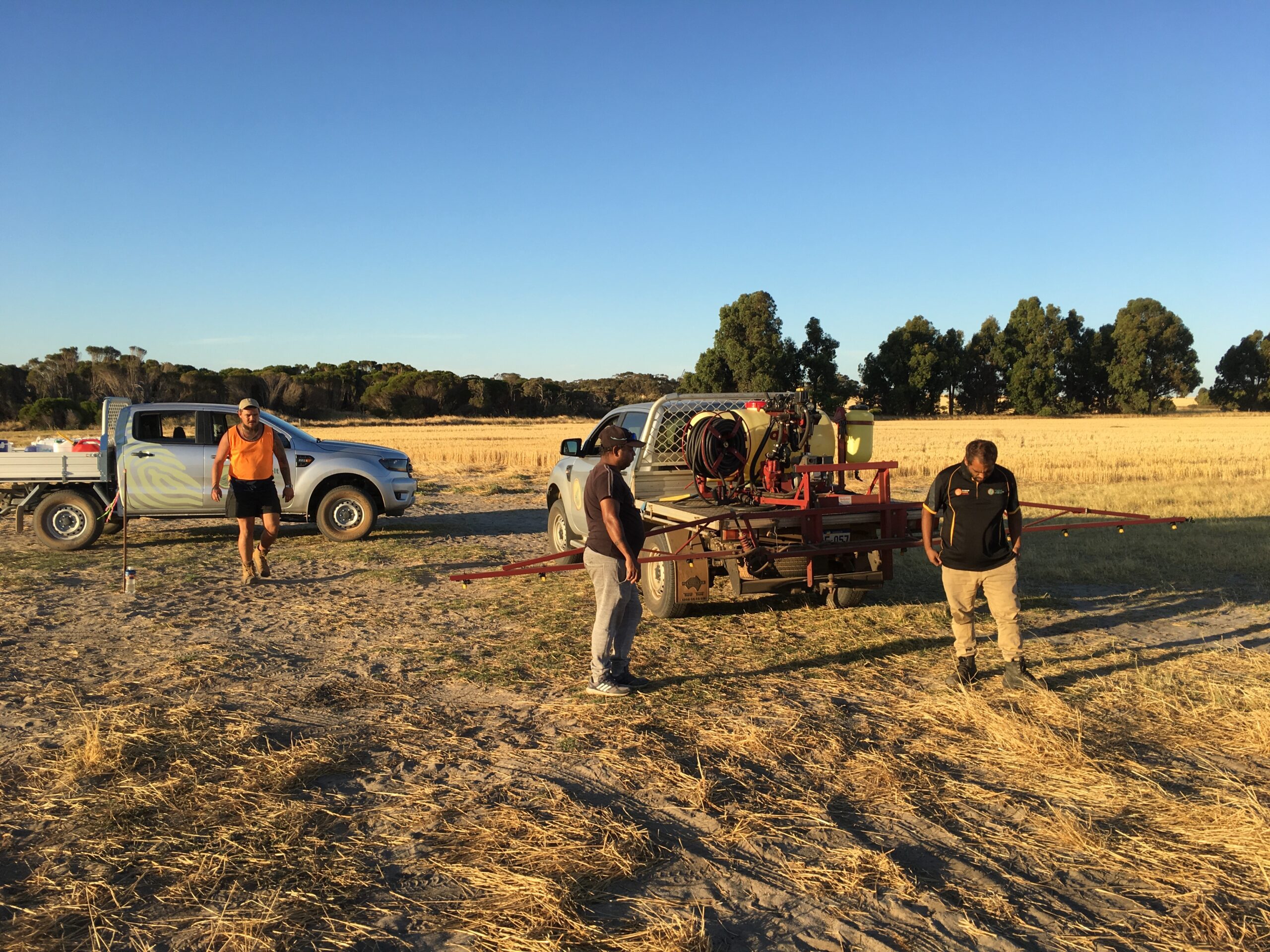 Three men standing around a mechanical spraying device mounted to the back of a ute