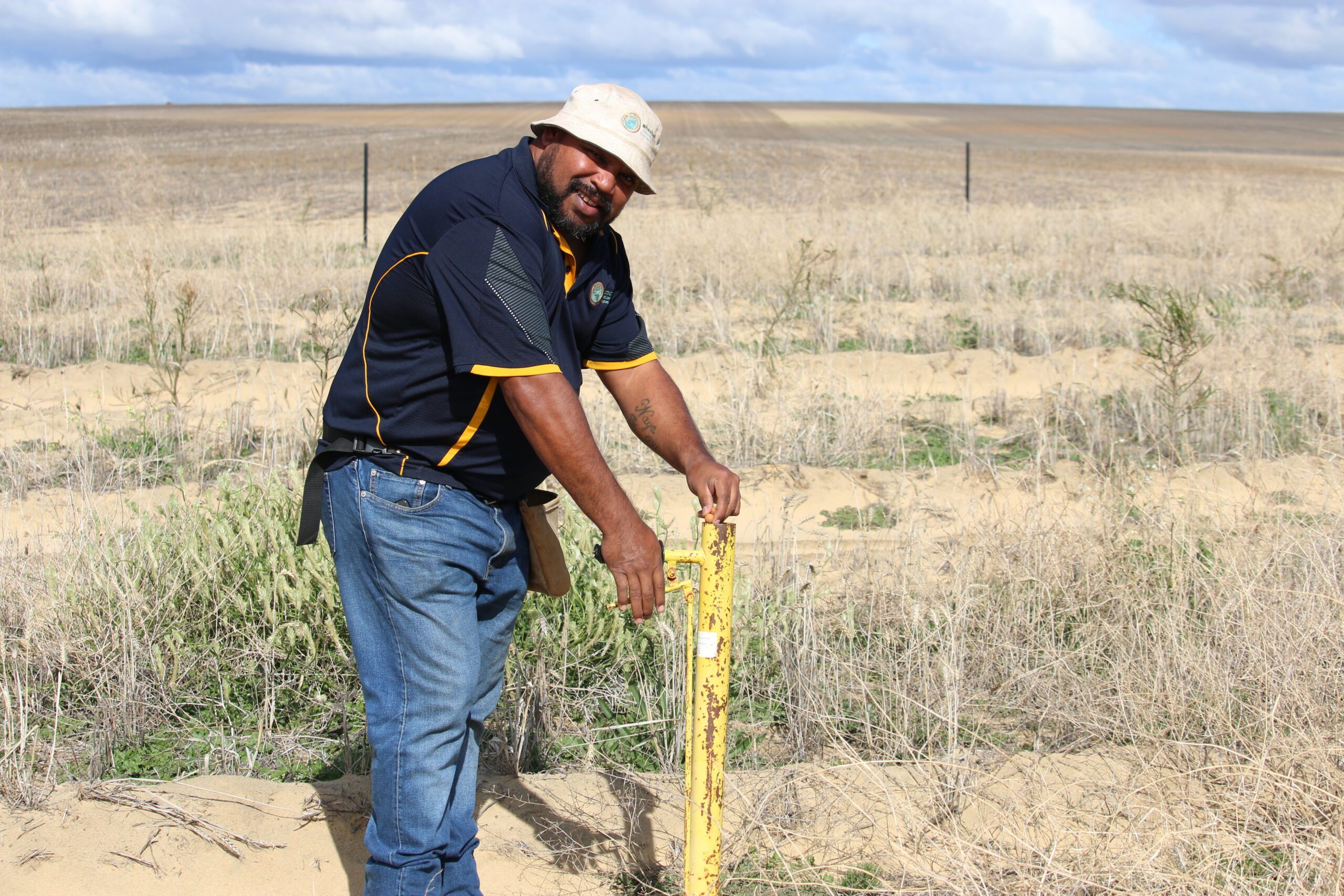 Man wearing a bucket hat using a pottiputki planting device to plant sandalwood seed