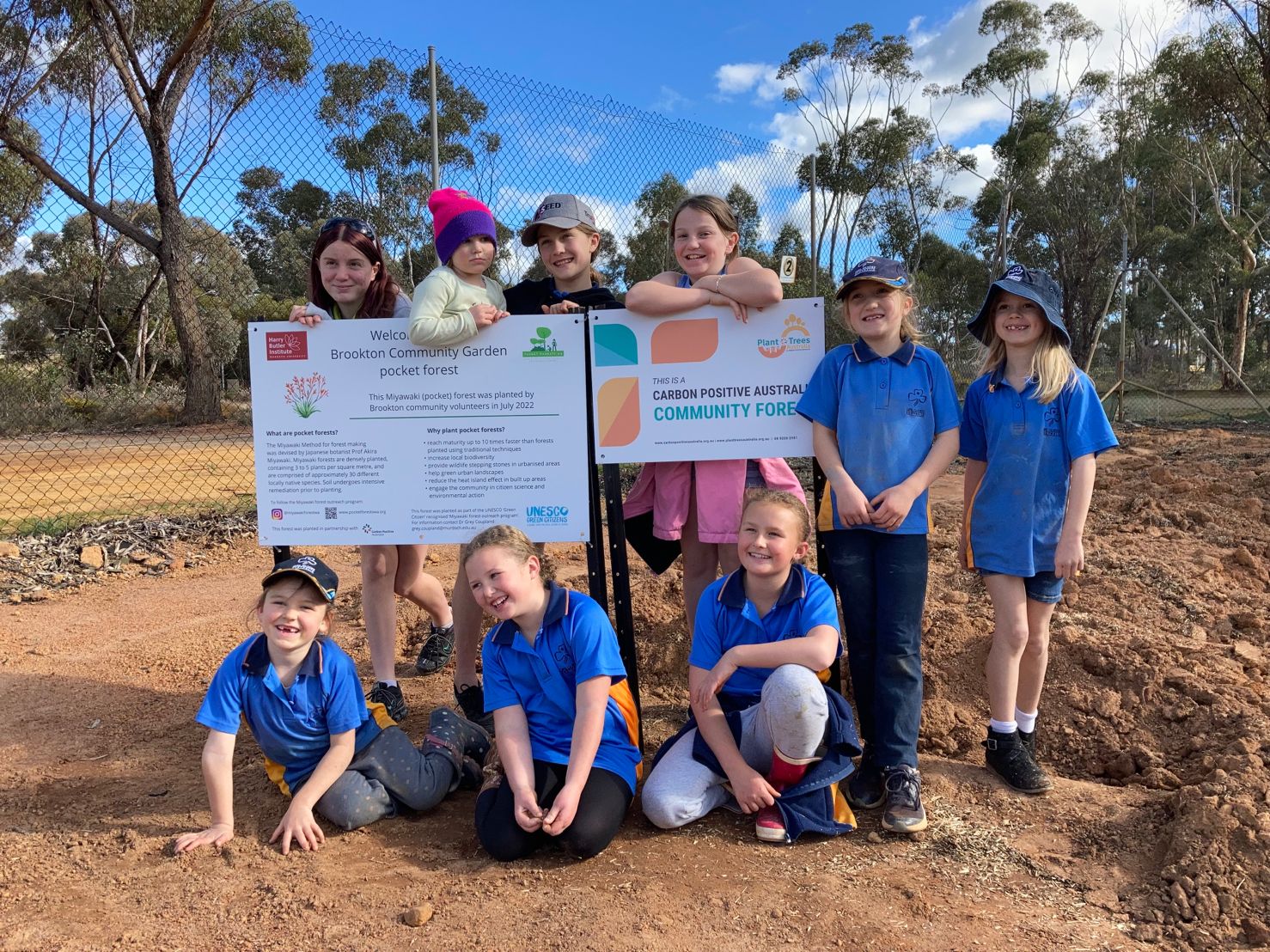 A group of school aged children standing around a sign that reads "This is a Carbon Positive Australia community forest"